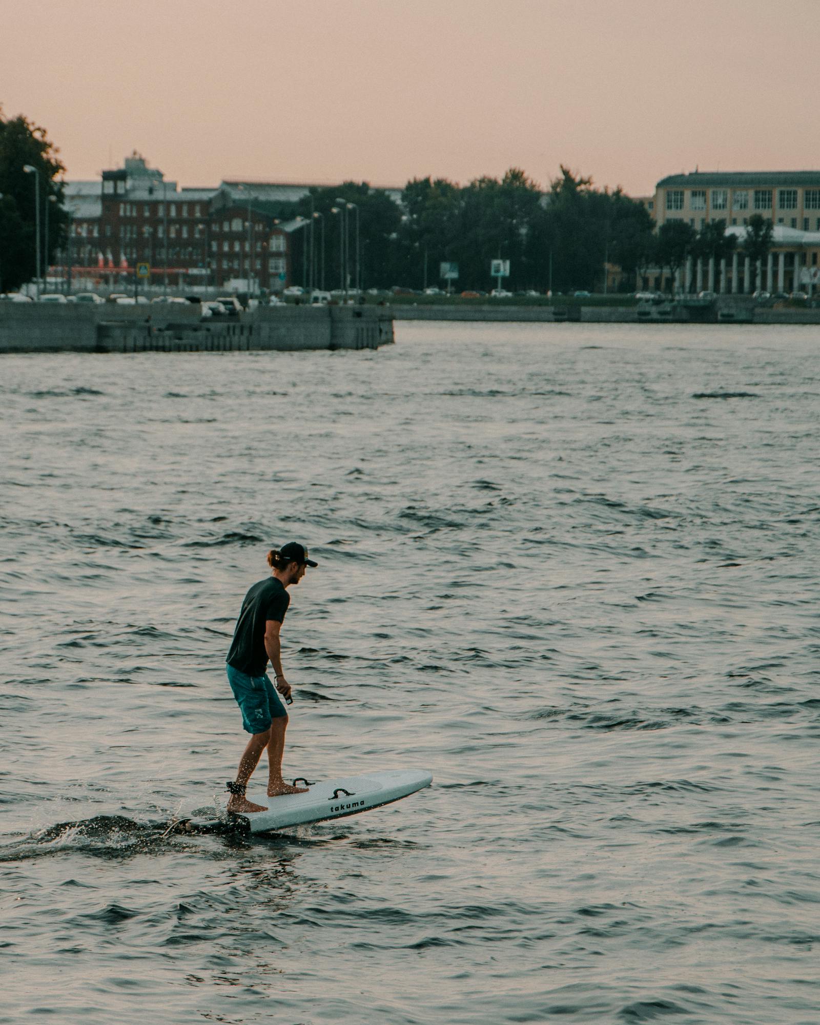 A rider on an electric hydrofoil board at golden hour, gliding above calm water.